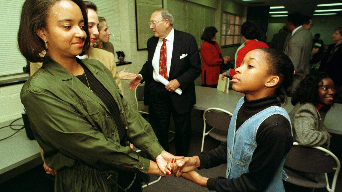 Donna Smith, left, then a family specialist with Ephesus Road Elementary school, holds hands with scholarship recipient Lakeisha Brown, then a fifth grader at the Chapel Hill school in this archival file photo. They were at a press conference where Harold Haidt (center background) and wife Elaine announced scholarships for students in the Blue Ribbon Mentor-Advocate program that make it through high school to college. Brown’s mentor, Pam Love of UNC, is seated at right.