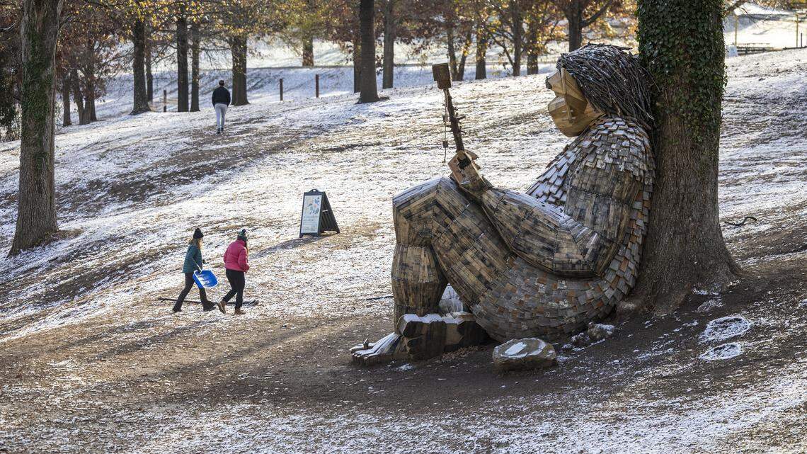Sophia Ashe, 14, and her mother, Kim Zdanowicz, head back up the slope at Dorothea Dix Park in Raleigh while attempting to sled in a dusting of snow that accumulated overnight on Tuesday morning, Dec. 9, 2025. A whimsical troll sculpture made from reclaimed wood by artist Thomas Dambo rests on the hillside.