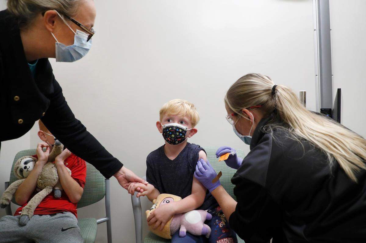 Kelly Baumberger of Apex holds the hand of her son Ethan, 5, as he gets a pediatric COVID-19 vaccine shot administered by Brigitta Bowers at UNC Children’s clinics in Raleigh, N.C., Thursday, Nov. 4, 2021. Son Lukas is to the left.