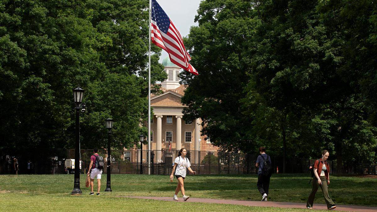 People walk through the campus of UNC-Chapel Hill near where a fence barrier surrounds the flagpole and portions of lawn on Friday, May 3, 2024.