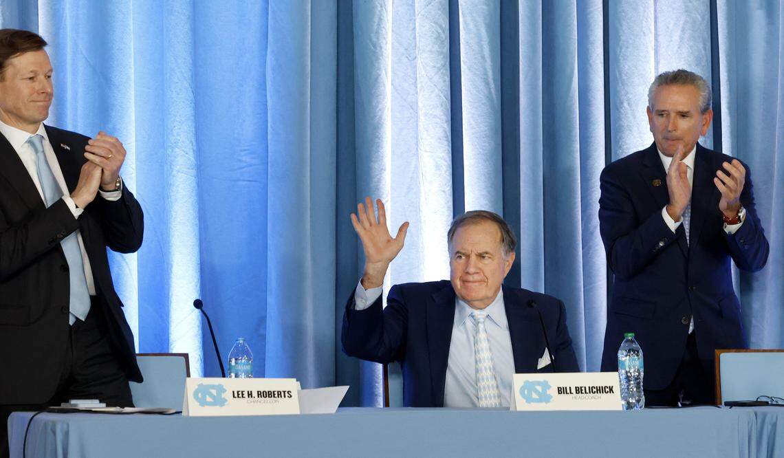 New North Carolina head football coach Bill Belichick (center) acknowledges the crowd at the start of the press conference announcing his hiring at the Loudermilk Center for Excellence at UNC in Chapel Hill, N.C., Thursday, Dec. 12, 2024. Chancellor Lee Roberts stands to the left and AD Bubba Cunningham stands to the right.