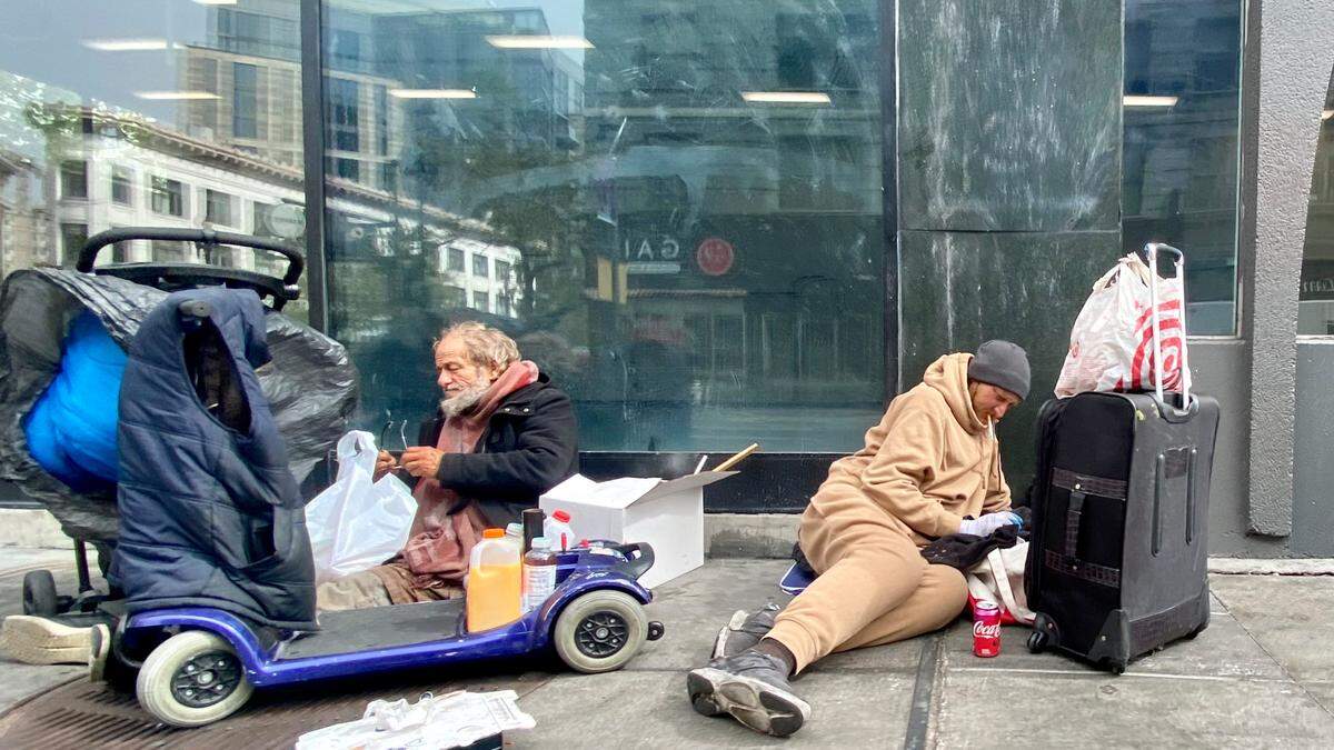 Two men sit with their belongings near the corner of Market St. and 6th St. in San Francisco on Wednesday. The area, known as the Tenderloin, is known for its large unhoused population, which some in the area say has become more of a problem in recent years.