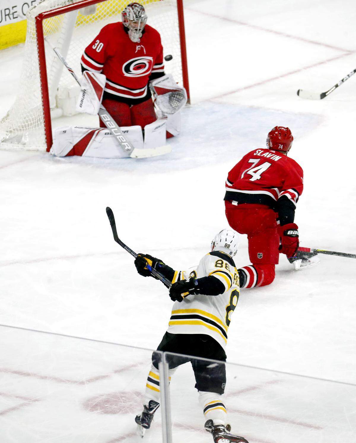The Bruins David Pastrnak (88) fires the puck past the Canes' Cam Ward (30) and Jaccob Slavin (74) for what proved to be the game winning goal during the third period of an NHL game played between the Carolina Hurricanes and the Boston Bruins at PNC Arena in Raleigh, N.C. on March 13,  2018.  The Bruins beat the Canes 6-4.
