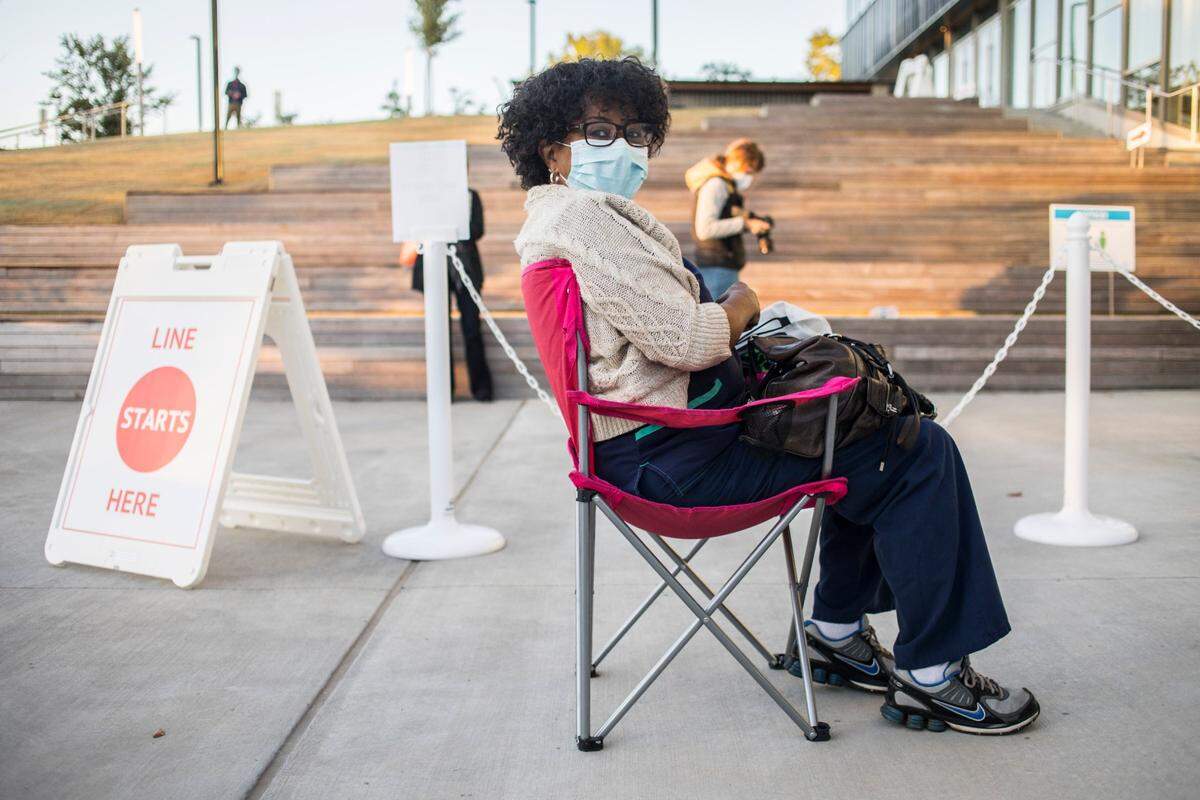 Enid Street sits close to the front of the long line of voters outside the Durham County Main Library in Durham, N.C. waiting to cast their votes on Thursday morning, Oct. 15, 2020, the first day of early voting.
