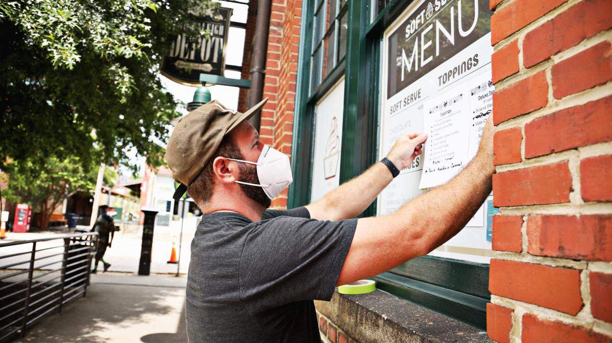 Many businesses adjusted to new difficulties during the COVID-19 pandemic. Pictured is Sam Ratto, co-founder of Videri Chocolate Factory in downtown Raleigh, posting the menu and hours for a new take-out window on Tuesday, Aug. 18, 2020.