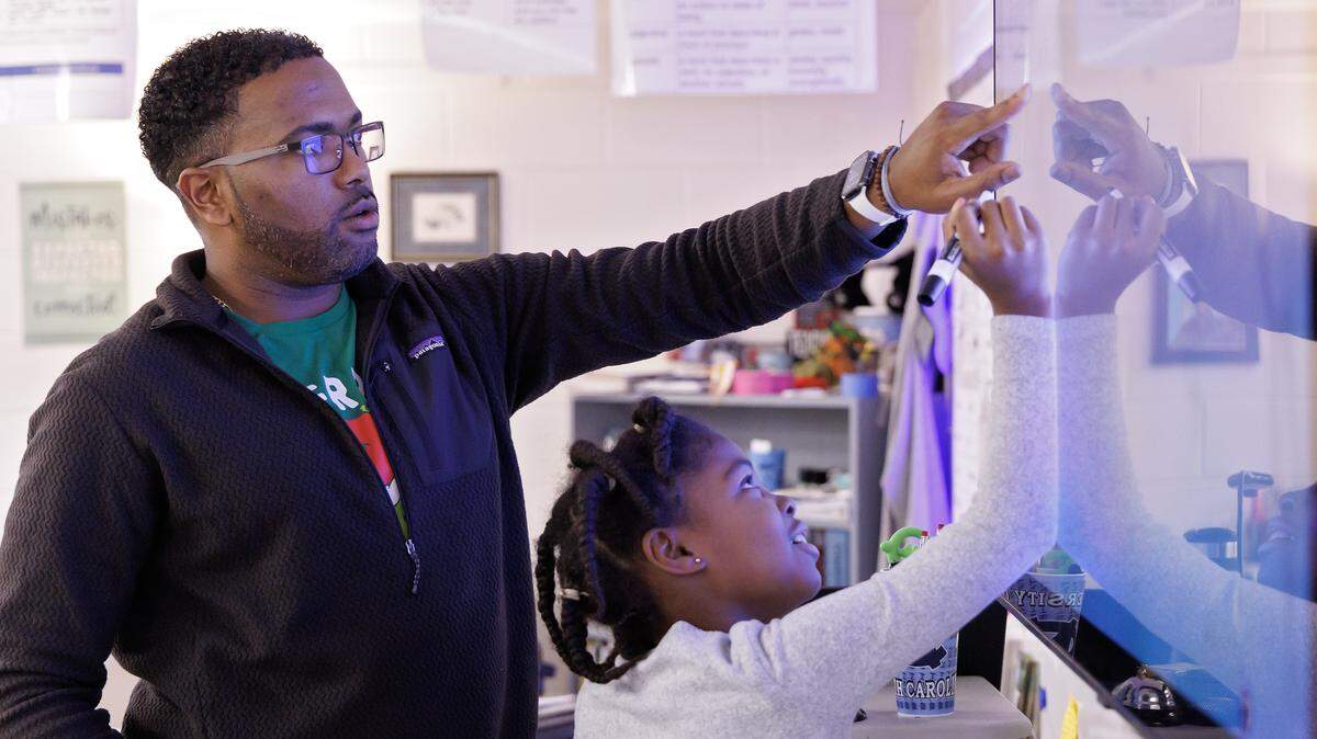 Pittsboro Elementary School fourth-grade teacher Shane Henderson, who recently won the Milken Educator Award, helps Nailah McMillan solve a problem during class. 