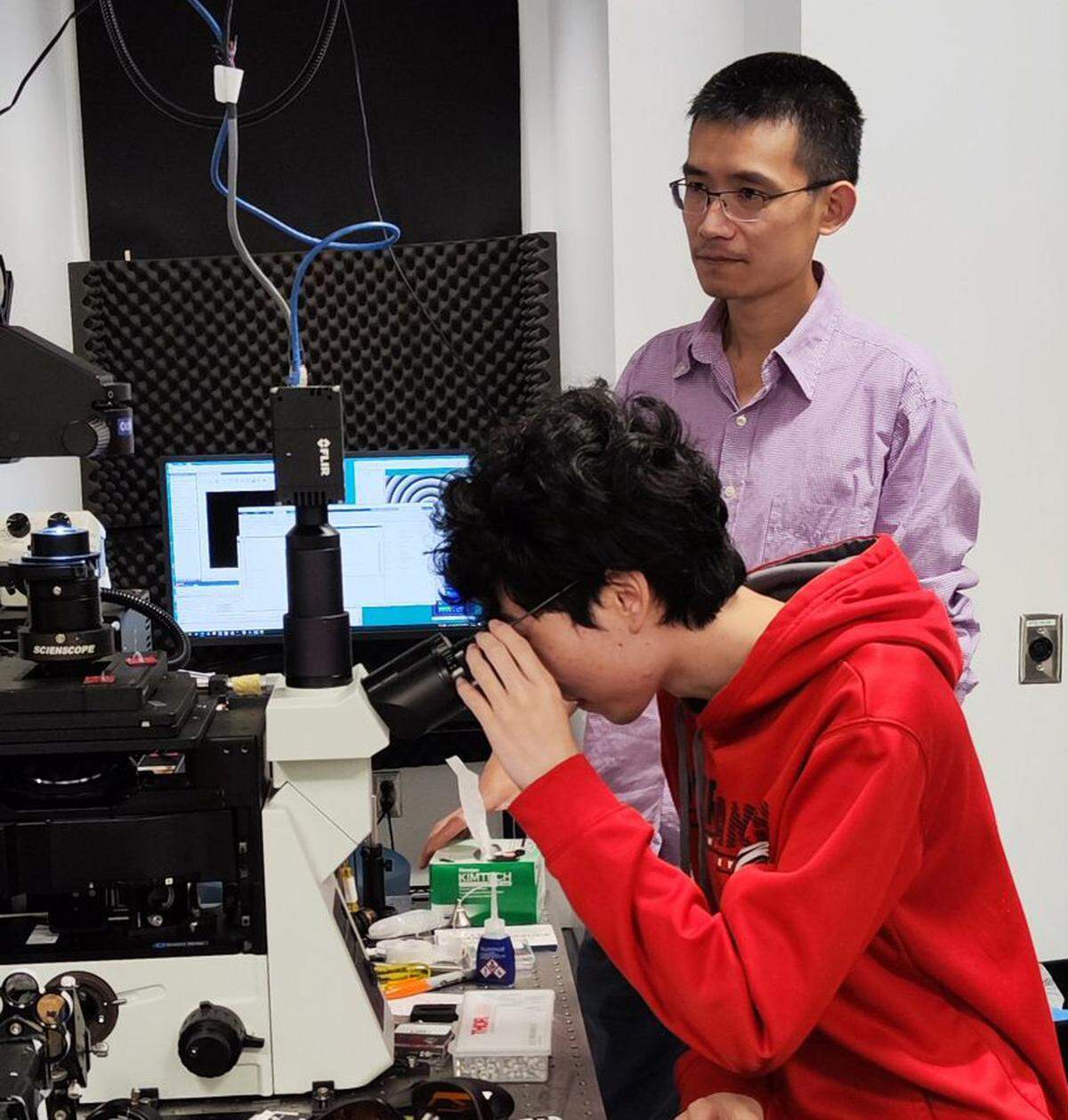 Zijie Yan (standing) and graduate student Anzhou Wen use an optical microscope to examine nanoparticles.