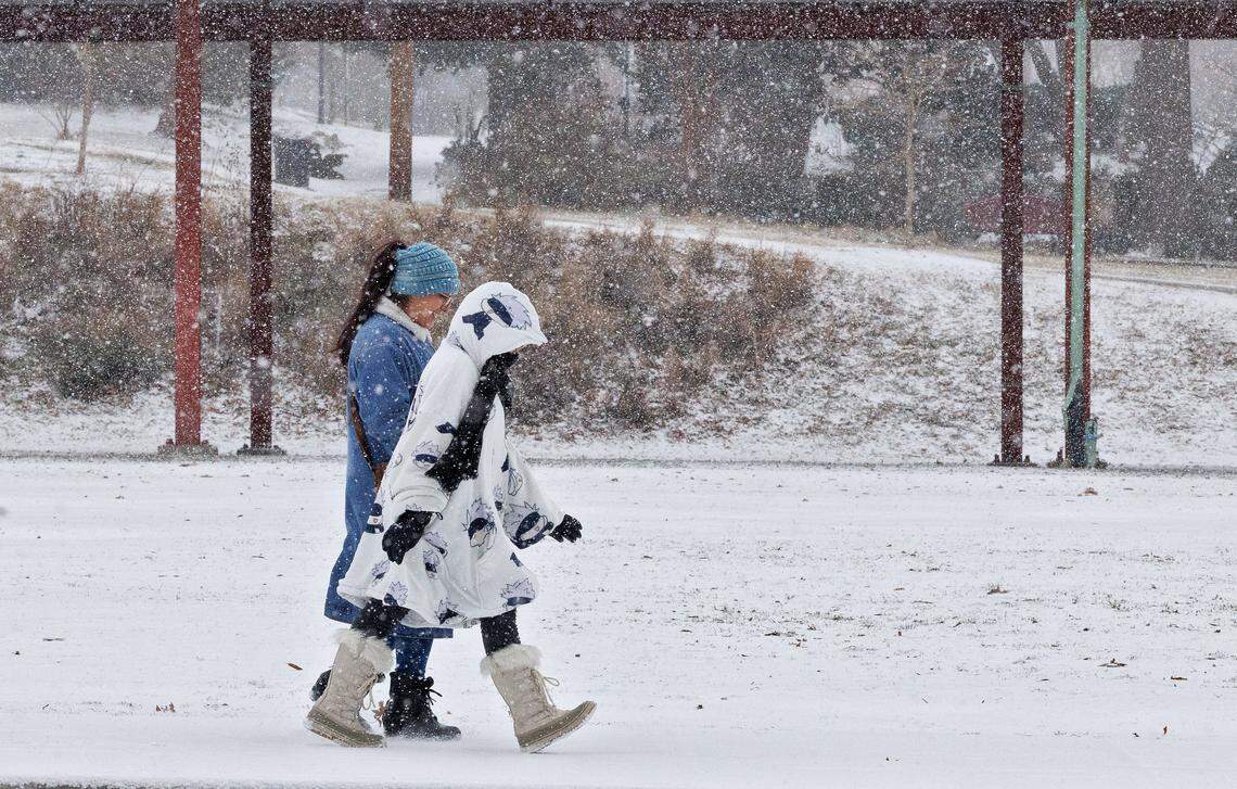 People walk along Foster Street as snow falls on Saturday, Jan. 31, 2026, in Durham, N.C.