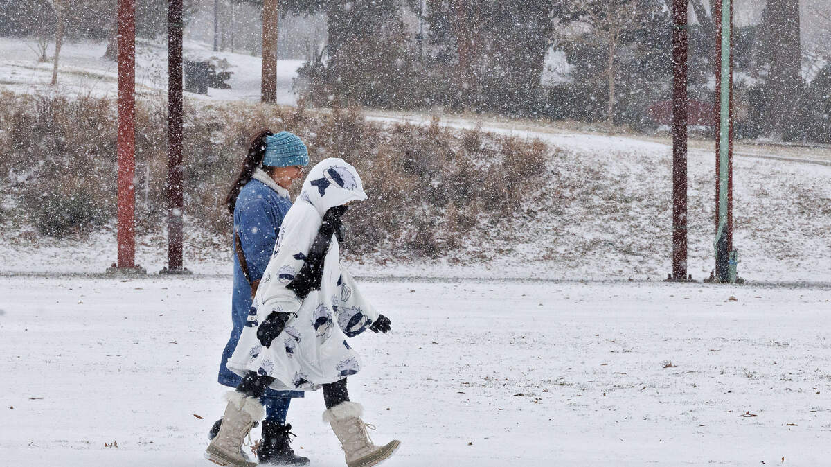 People walk along Foster Street as snow falls on Saturday, Jan. 31, 2026, in Durham, N.C.