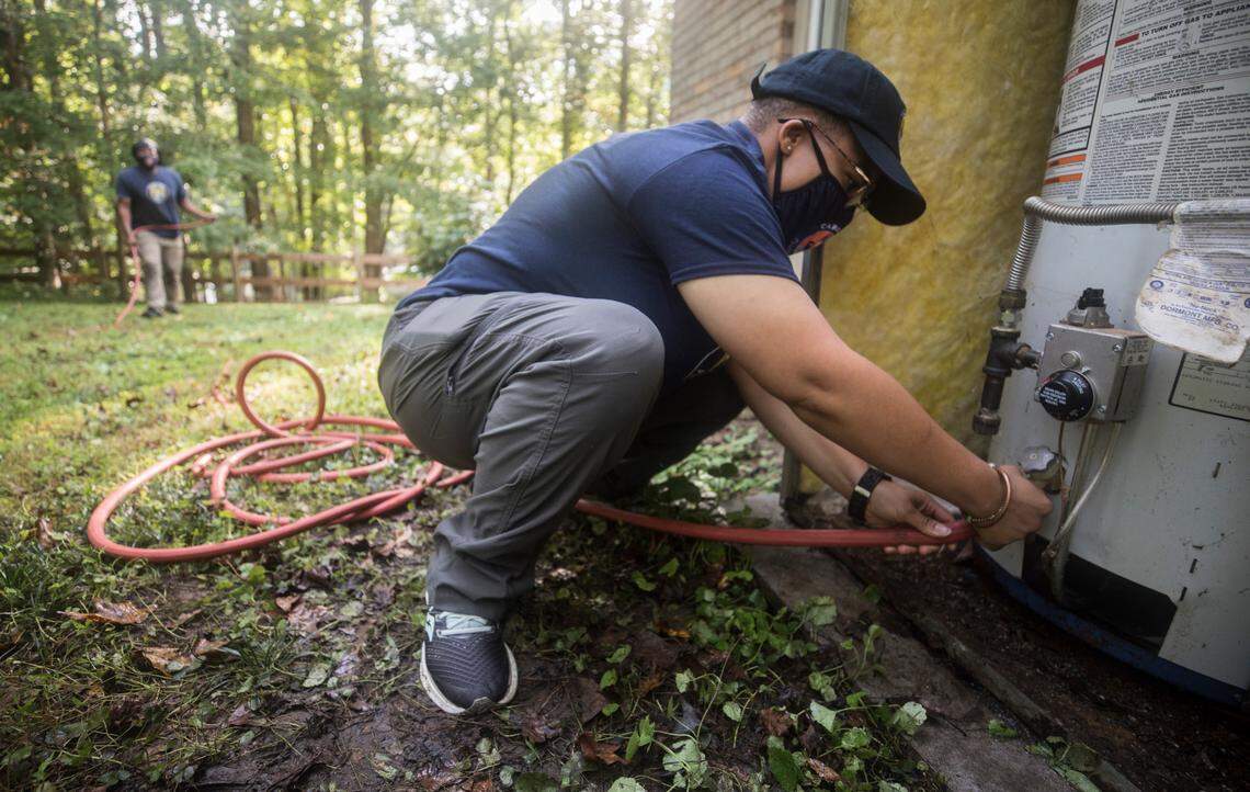 Jasmine Jones works on a water heater at a home in Durham, N.C. on Tuesday, Sept. 29, 2020, her second day as an employee of Carrboro Plumbing, Inc. Her co-worker, Corey Rone, left, is helping her learn on the job. Jones received training in the plumbing trade from Hope Renovations, a program aimed at helping women learn trades that will lead to future employment.