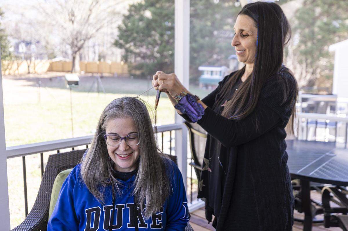 Leslie Stern applies fairy hair, metallic-like threads of tinsel, to her friend Liz Buno’s hair without compensation as a personal arrangement at Stern’s home in Durham.