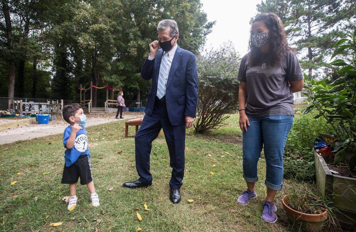 Gov. Roy Cooper talks with a child and teacher Kristi Royster, right, at the Community School for People Under Six in Carrboro, N.C., on Thursday, Oct. 7, 2021.