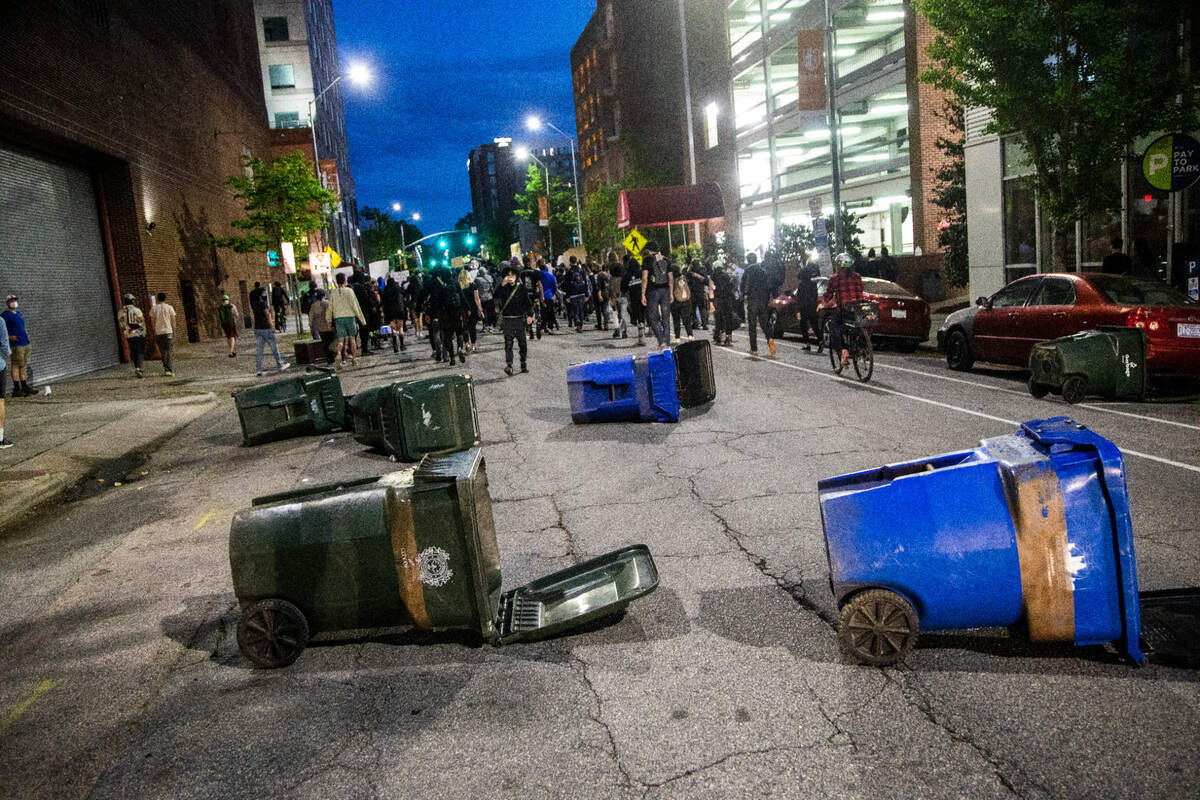 Demonstrators leave trash and recycling bins in the street while being followed by police vehicles as they march in downtown Raleigh after a vigil for Daunte Wright and others killed by police Sunday, April 18, 2021. At least 8 people were arrested.