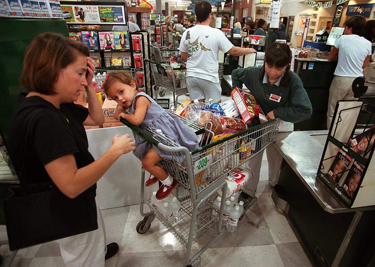 Ann Vitti does a quick inventory of her shopping cart after waiting in the checkout line at the Cameron Village Harris Teeter grocery store in Raleigh, NC. Daughter Julia, 2, waits in the cart. Triangle residents crowded hardware and grocery stores to purchase food, water, flashlights, chain saws, batteries and tarps in preparation for the possible arrival of Hurricane Floyd. Harris Teeter had a run on batteries and bottled water. Harris Teeter employee Moo Hayes prepares to unload the shopping cart. staff/scott sharpe