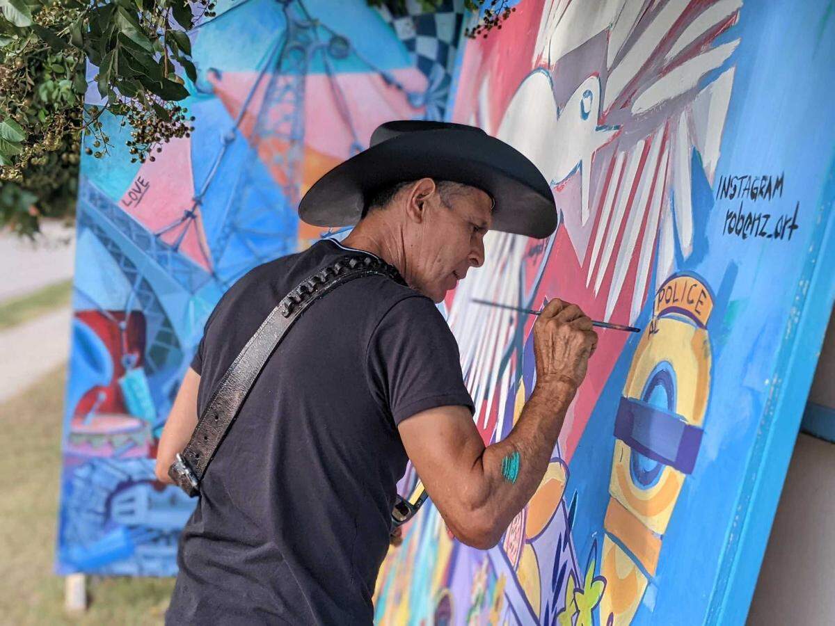 Dallas-based artist named Roberto Marquez paints a mural near the entrance of the Hedingham neighborhood in Raleigh, N.C., on Oct. 17, 2022. Marquez wanted to honor the five people killed in the mass shooting Oct. 13, 2022.