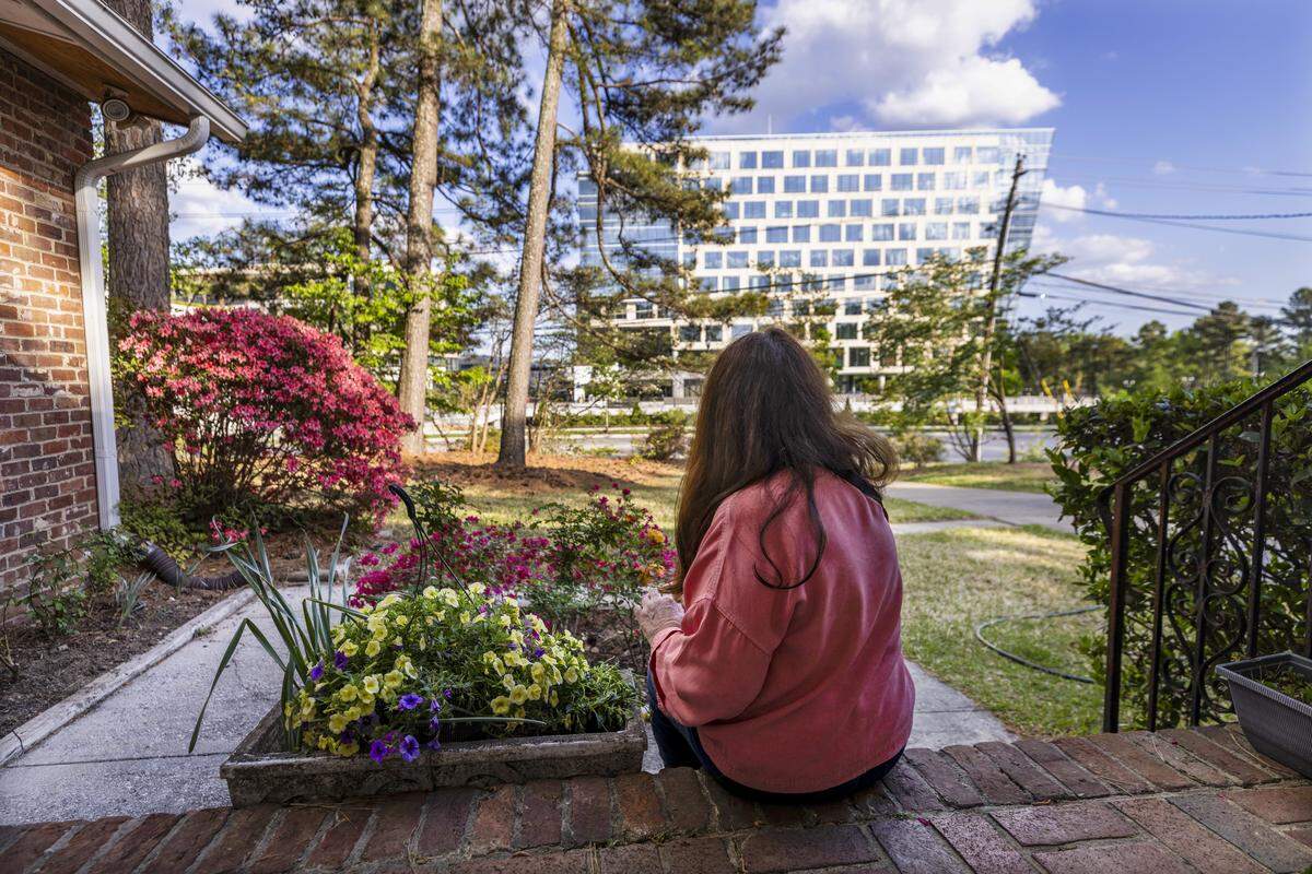 Residents along Lassiter Mill Road are concerned that recent developments by Kane Realty Corp. in Raleigh’s North Hills district are encroaching on their homes. Another office building is under construction between the home in this photo and the tower in the background.