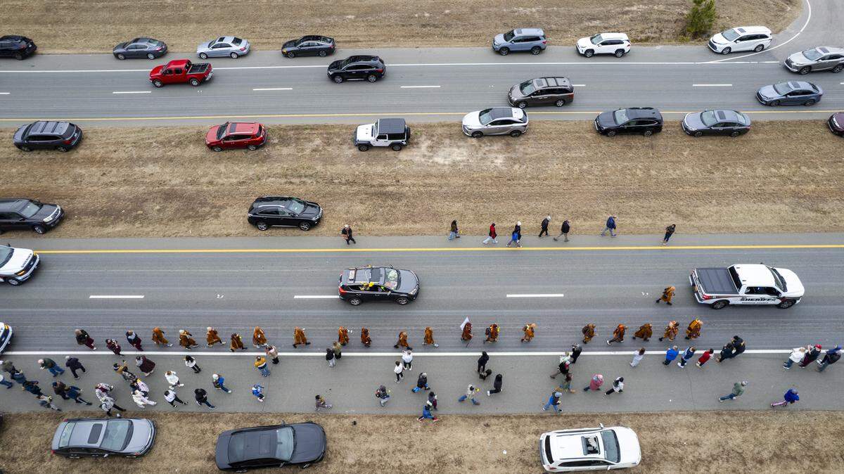 A procession of Buddhist monks walks along U.S. Highway 64 near Wilsonville on Friday, Jan. 23, 2026, as thousands of onlookers line the highway to welcome them. The monks are making a 2,300-mile pilgrimage from Texas to Washington, D.C., as part of the Walk for Peace, an effort to promote peace, compassion and national unity.