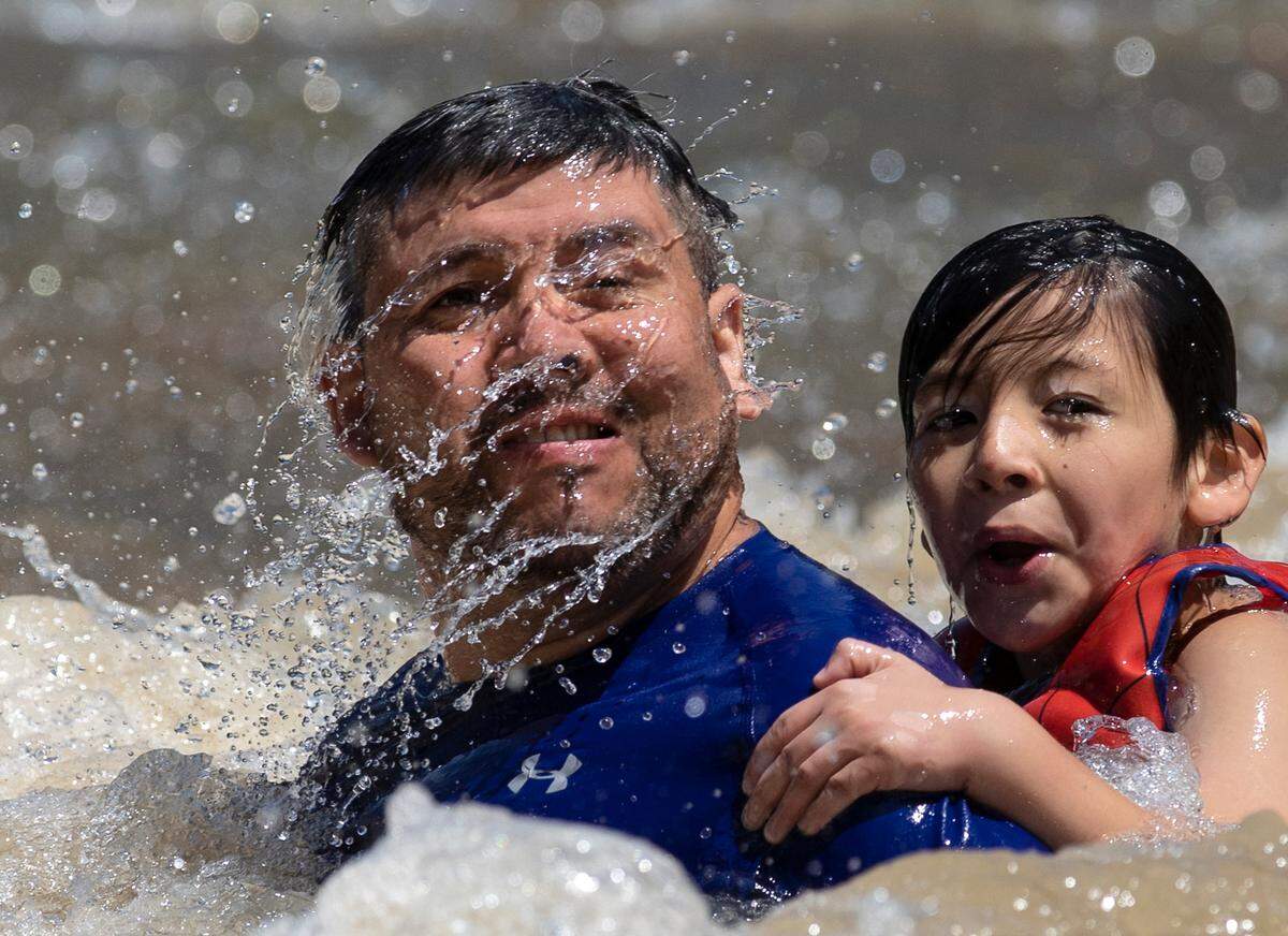 Manuel Yañez and his son, Eithan, 7, emerge from the water after sliding down a rock face at RiverPark at Cooleemee Falls on Saturday, Aug. 5, 2023, in Woodleaf, N.C.