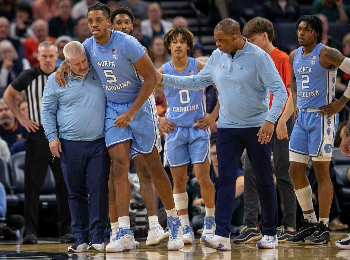 North Carolina trainer Doug Halverson and coach Hubert Davis help Armando Bacot (5) off the court after an injury in the opening minutes of play against Virginia on Tuesday, January 10, 2023 at John Paul Jones Arena in Charlottesville, Va.