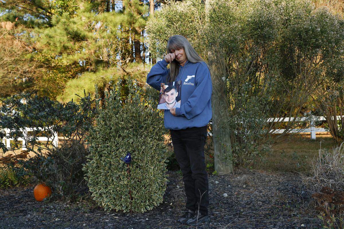 Lisa Higgins holds a photograph of her son, Michael Higgins, while standing next to his roadside memorial in November. Michael, a Highway Patrol intern, died after a trooper reached 113 mph and lost control of his patrol car on a rural Pitt County road in August 2020.