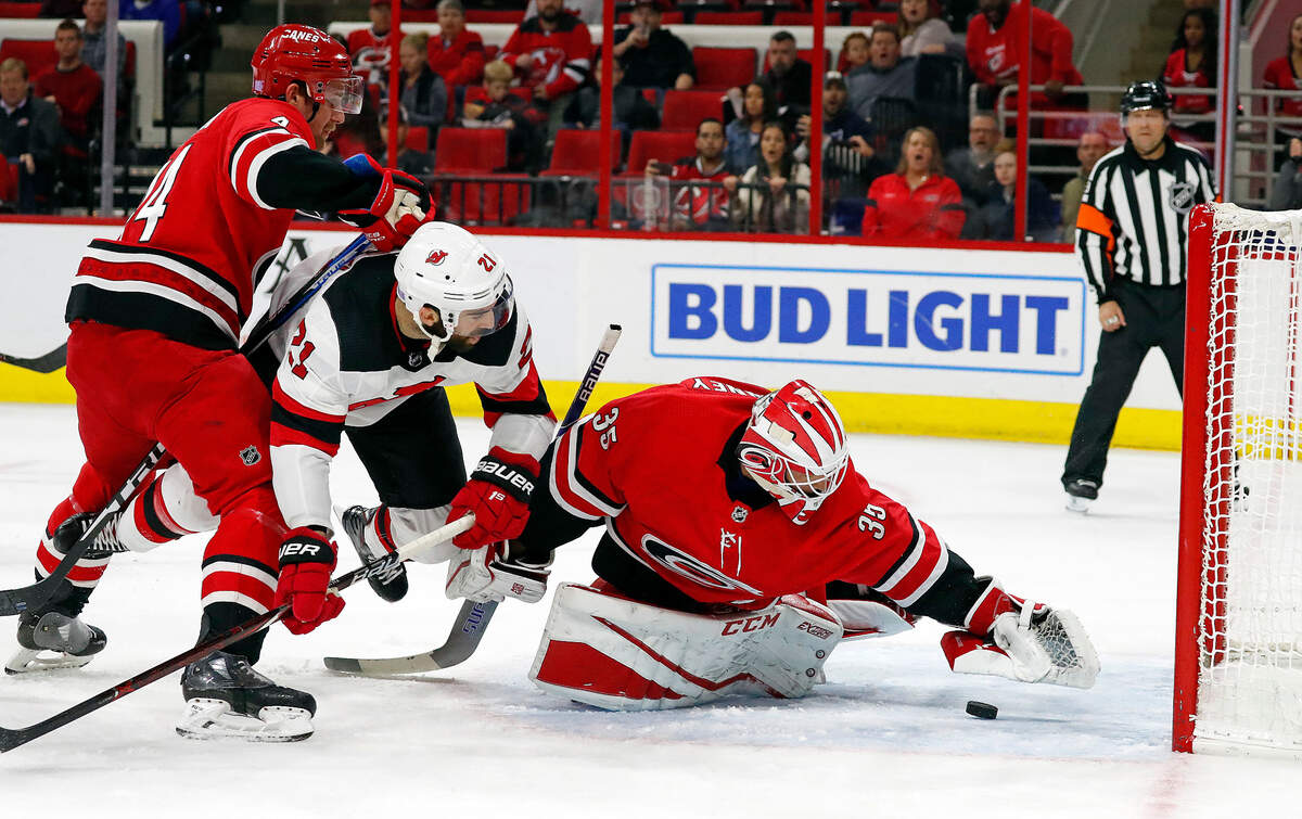 Carolina Hurricanes goaltender Curtis McElhinney (35) reaches for the puck in front of New Jersey Devils’ Kyle Palmieri (21) and Hurricanes’ Calvin de Haan (44) during the first period of an NHL hockey game Sunday, Nov. 18, 2018