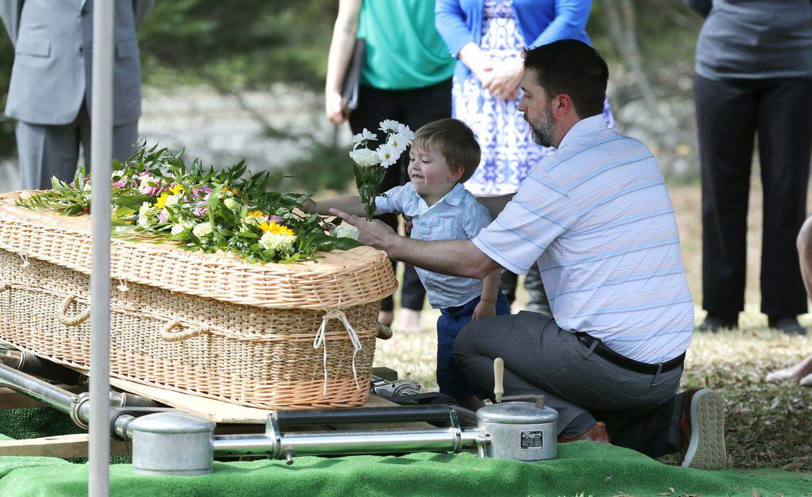 Andy Medlin helps his son Drew, 2, put a flower on the seagrass wicker casket of Andy’s mother, Doris Medlin, during a graveside service at the Historic Oakwood Cemetery in Raleigh, N.C., Friday, March 20, 2020.