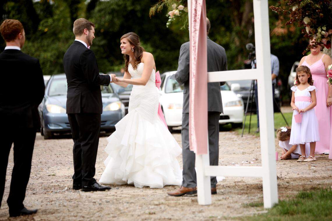 Carrie McQuaid, center, leans into her groom, John Michael Simpson, left, as they prepare to say their vows during their wedding ceremony on Sunday, Sept. 27, 2020, in Youngsville. The couple decided to have their ceremony in the parking lot of the Victorian House so that they could invite more guests who could watch from their cars. They also live-streamed the wedding for others who couldn’t attend in person.