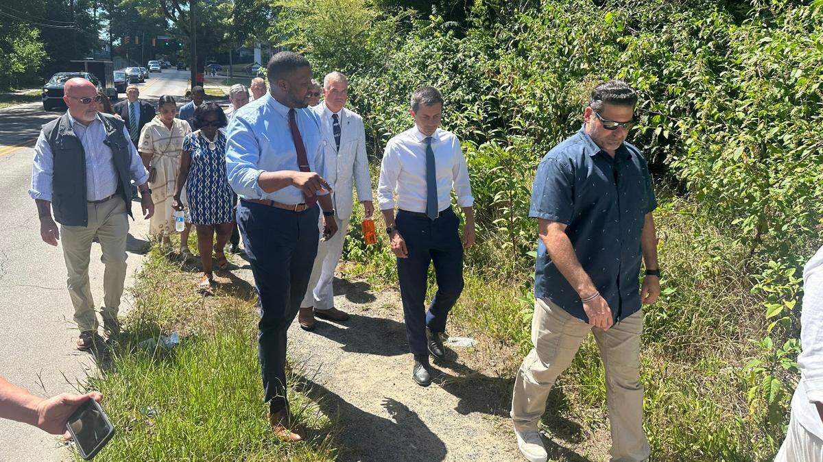 Durham Mayor Leonardo Williams and U.S. Transportation Secretary Pete Buttigieg walk on a gravel path along Holloway Street on Tuesday, July 2. The city will build sidewalks, crosswalks and new bus shelters along 2 miles of Holloway using a $12 million federal grant Buttigieg announced a few days earlier.