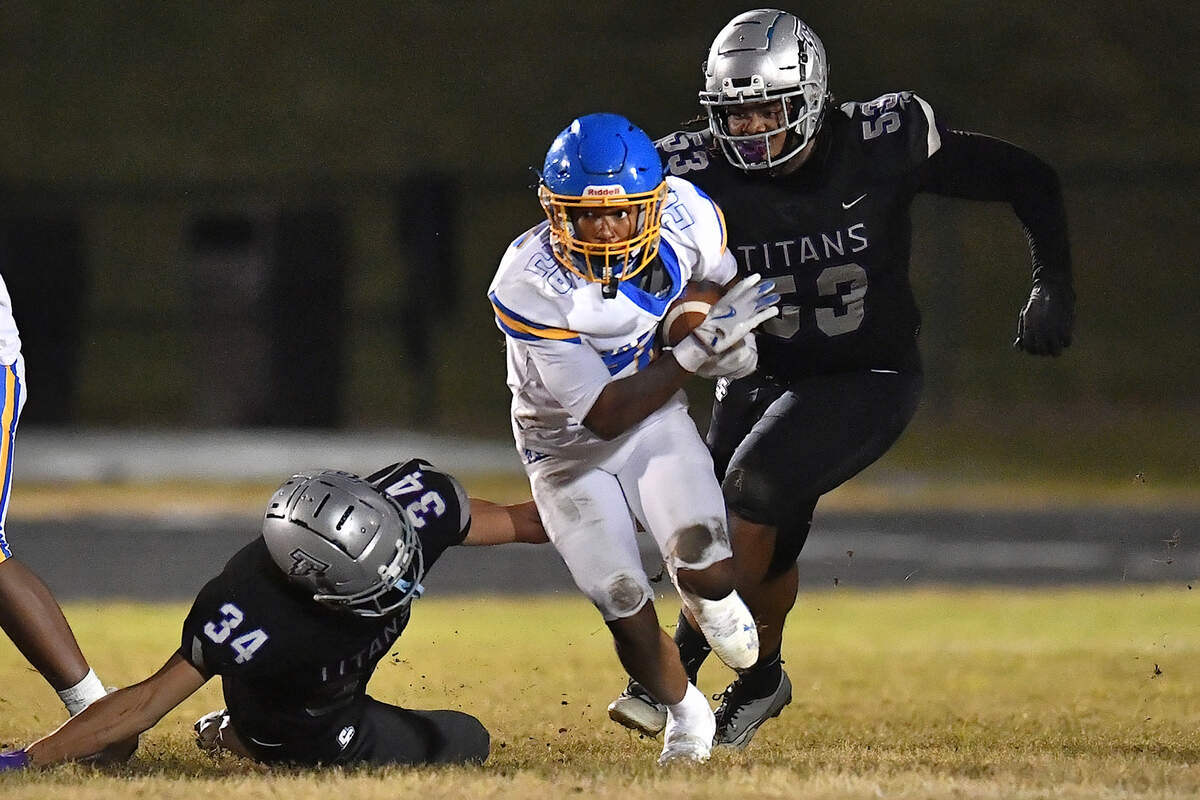 Garner running back Austin Williams (26) runs for yardage past South Garner's 	Kenneth Cruz (34) and Dezmere Johnson (53) during the first half. The South Garner Titans and the Garner Trojans met in a conference football game in Raleigh, N.C. October 17, 2025