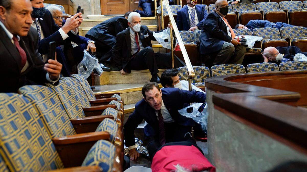 People shelter in the House gallery as protesters try to break into the House Chamber at the U.S. Capitol on Wednesday, Jan. 6, 2021, in Washington.