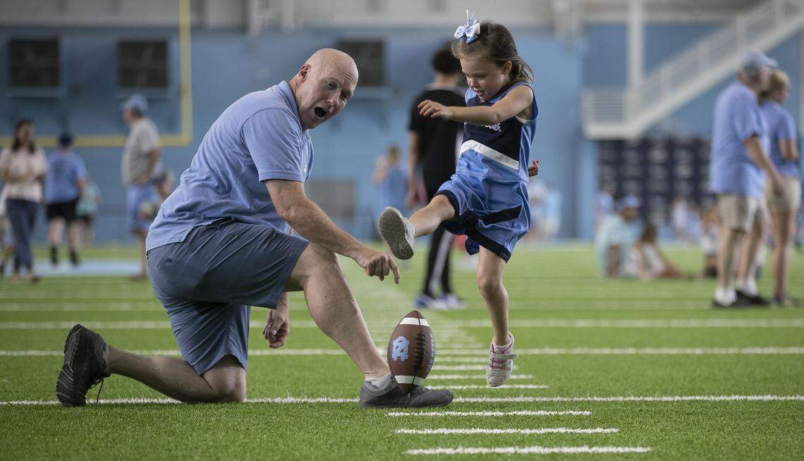 Tim Tompkins of Raleigh, N.C. acts as a place holder for his six-year-old daughter Arabella Tompkins as she practices her field goal kicking form during the annual Meet The Heels event on Saturday, August 3, 2019 at the Football Practice Complex in Chapel Hill, N.C.