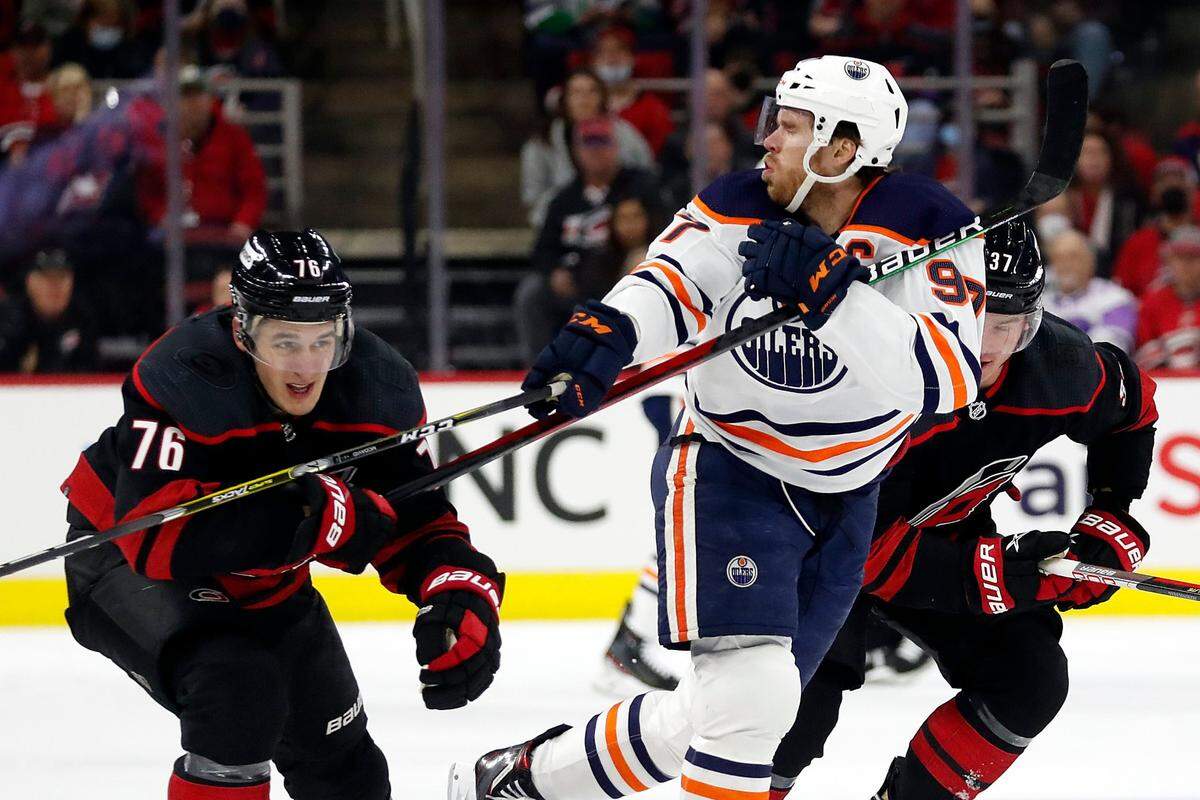 Edmonton Oilers’ Connor McDavid (97) takes a high stick from Carolina Hurricanes’ Brady Skjei (76) during the first period of an NHL hockey game in Raleigh, N.C., Sunday, Feb. 27, 2022. (AP Photo/Karl B DeBlaker)