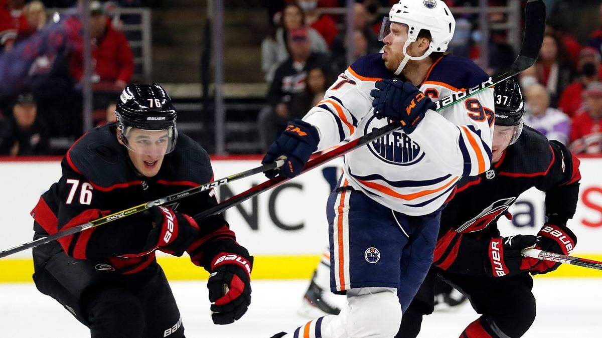 Edmonton Oilers’ Connor McDavid (97) takes a high stick from Carolina Hurricanes’ Brady Skjei (76) during the first period of an NHL hockey game in Raleigh, N.C., Sunday, Feb. 27, 2022. (AP Photo/Karl B DeBlaker)