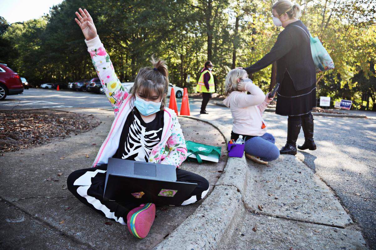 Abby Neblett, 8, left, raised her hand during an online class while her sister, Emily, 10 attends class via cellphone as they wait in line with their mom, Katherine, during early voting at Lake Lynn Community Center in Raleigh on Thursday morning, Oct. 15, 2020. Neblett says she wanted to bring her daughters to witness this moment in history so they would understand how important it is to vote.