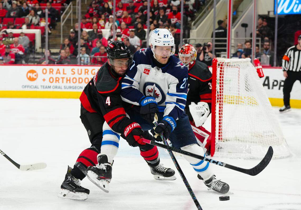 Mar 9, 2025; Raleigh, North Carolina, USA;  Carolina Hurricanes defenseman Shayne Gostisbehere (4) and Winnipeg Jets left wing Nikolaj Ehlers (27) battle over the puck during the second period at Lenovo Center. Mandatory Credit: James Guillory-Imagn Images