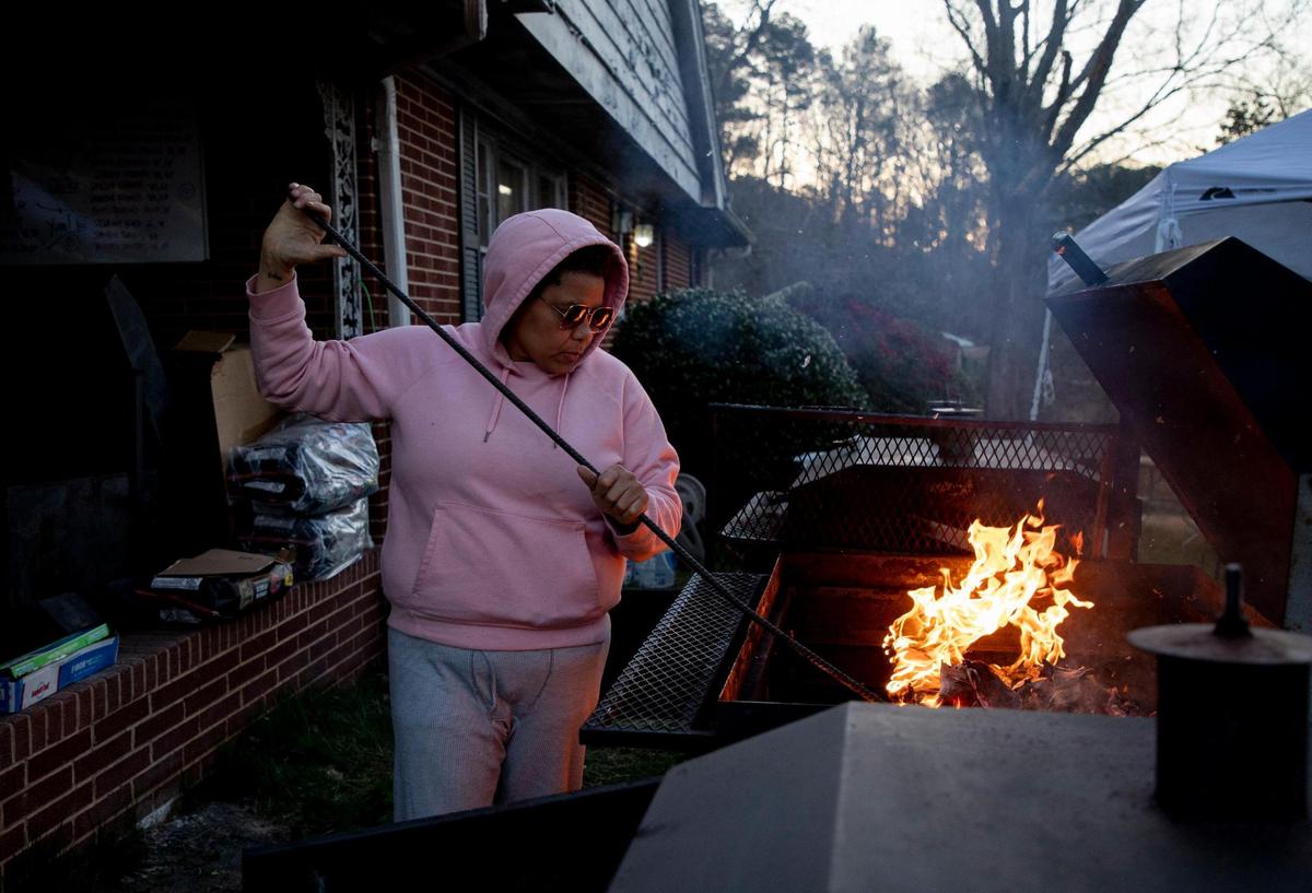 Katina Parker builds a fire in a smoker early in the morning on the second day of the five-day no-contact cookout known as Feed Durham that began as a response to the increase of food insecurity at the start of coronavirus pandemic, bringing dozens of volunteers to her front yard every six to eight weeks to cook well-seasoned and nutrient-dense meals for people in need, on Wednesday, Mar. 3, 2021, in Durham, N.C.