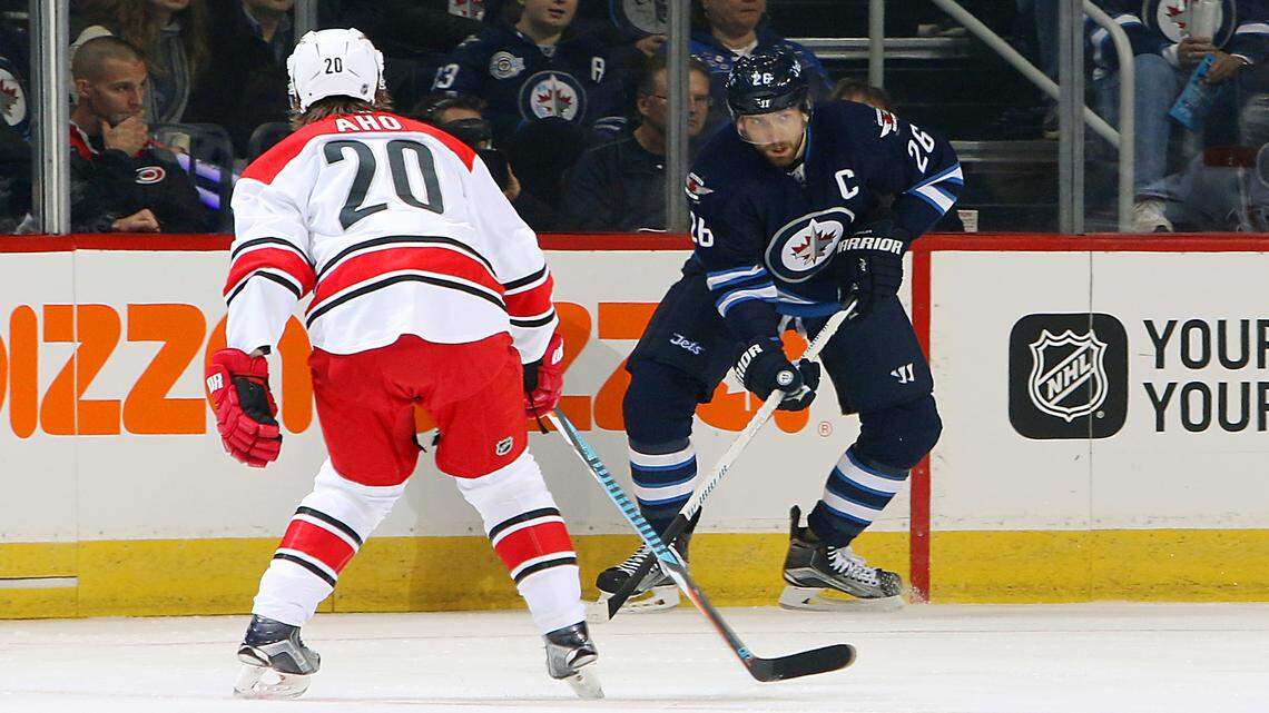 Blake Wheeler (26) of the Winnipeg Jets plays the puck along the boards as Sebastian Aho (20) of the Carolina Hurricanes defends during first period at the MTS Centre. 