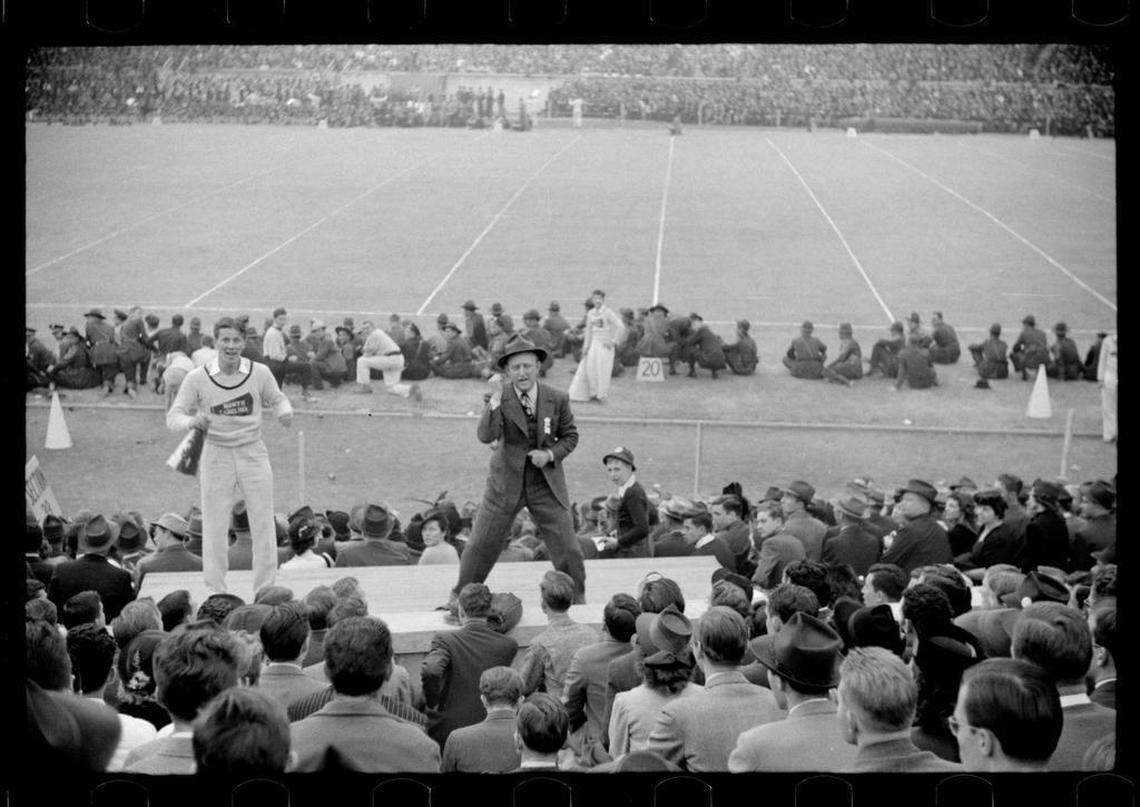 Fans ringed the sidelines and famous bandleader Kay Kyser (right) and a UNC cheerleader lead the crowd in cheers at the 1939 Duke-Carolina game played in Durham, NC. UNC’s mascot “Rameses” can be seen just behind the cheerleader.