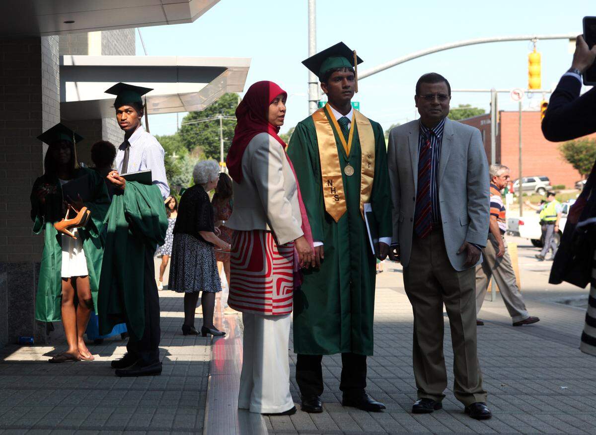 Khari Bailey, 18, left, watches as Farah Khan, 18, poses for a picture with his mother, Nasrin Khan, 42, left, and his father, M. Khan, 54, after Enloe High School held a Sunday morning graduation ceremony in 2014 in the Raleigh Convention Center.