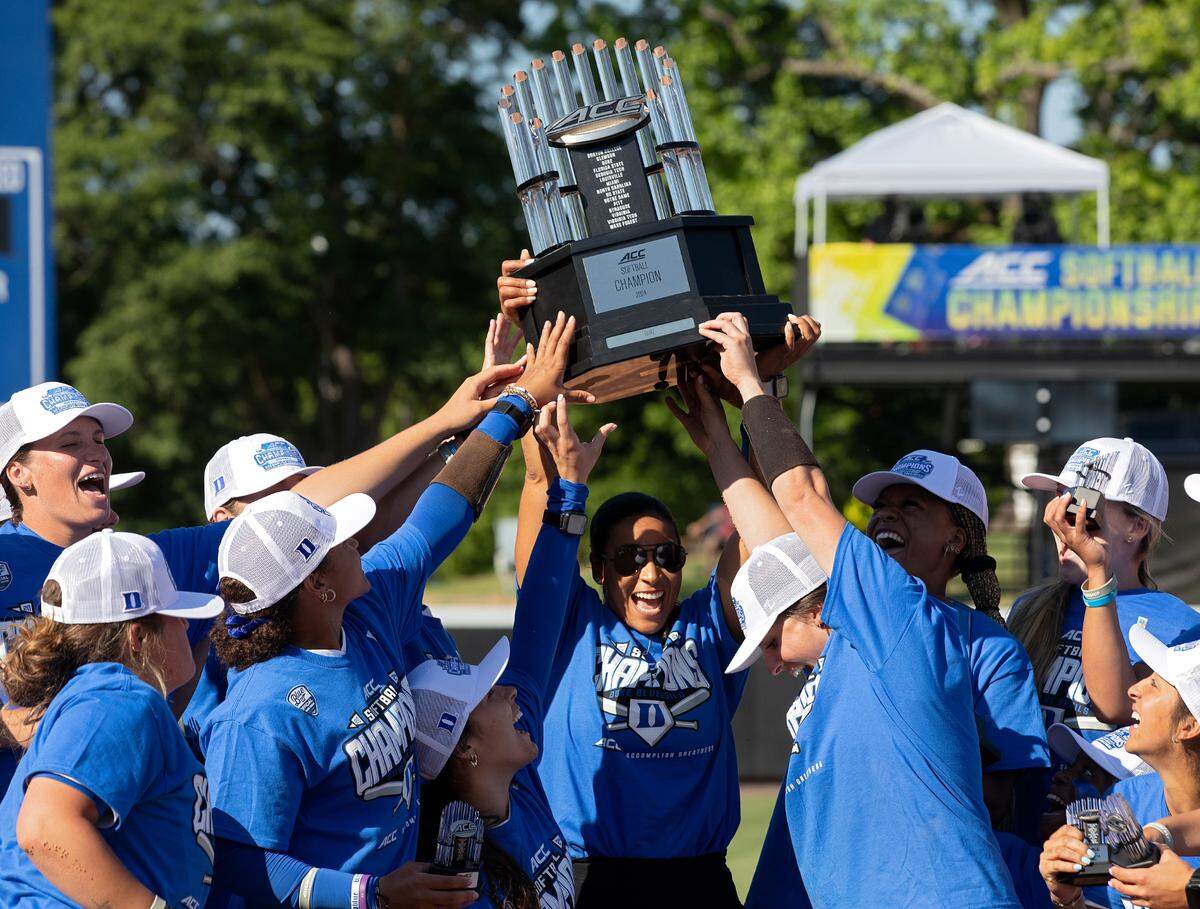 Duke head coach Marissa Young, center, hoists the ACC Tournament trophy following the Blue Devils’ 6-3 win over Florida State on May 11, 2024, in Durham. After her husband suffered a heart attack, Young led her team to its best season in its seven-year history.
