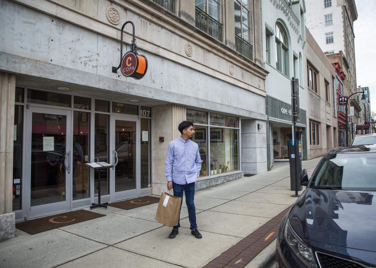 Brian Perez, a server at Copa, waits to give a customer a to-go order curbside as the restaurant trains its staff on the workflow of filling an increasing number of to-go orders and offering curbside service, in response to preventing the spread of COVID-19, on Friday, March 13, 2020, in Durham, N.C.