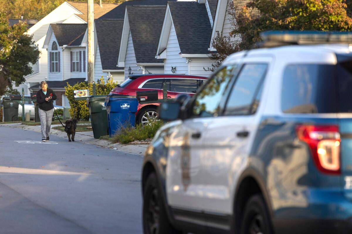A resident in the Hedingham neighborhood walks their dog on Castle Pines Drive Friday morning, October 14, 2022 in Raleigh, N.C. as law enforcement continue to investigate the killing of five people yesterday on the greenway nearby.