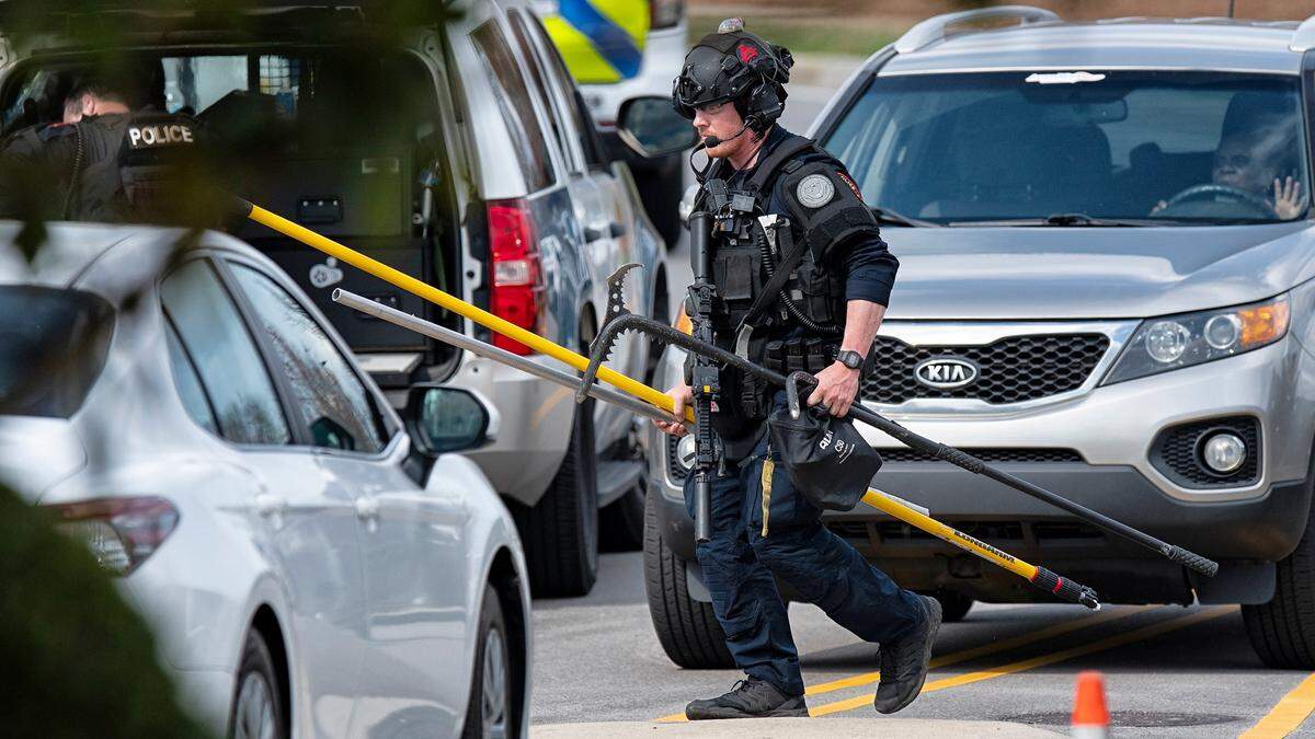 A police officer wearing tactical gear carries a long gun and other equipment to the scene of a standoff at the Windsor Apartments in Cary, N.C., Wednesday, Feb. 22, 2023. Cary police say said a man is still barricaded inside the home, but the juvenile is being treated at a hospital after suffering gunshot wounds.