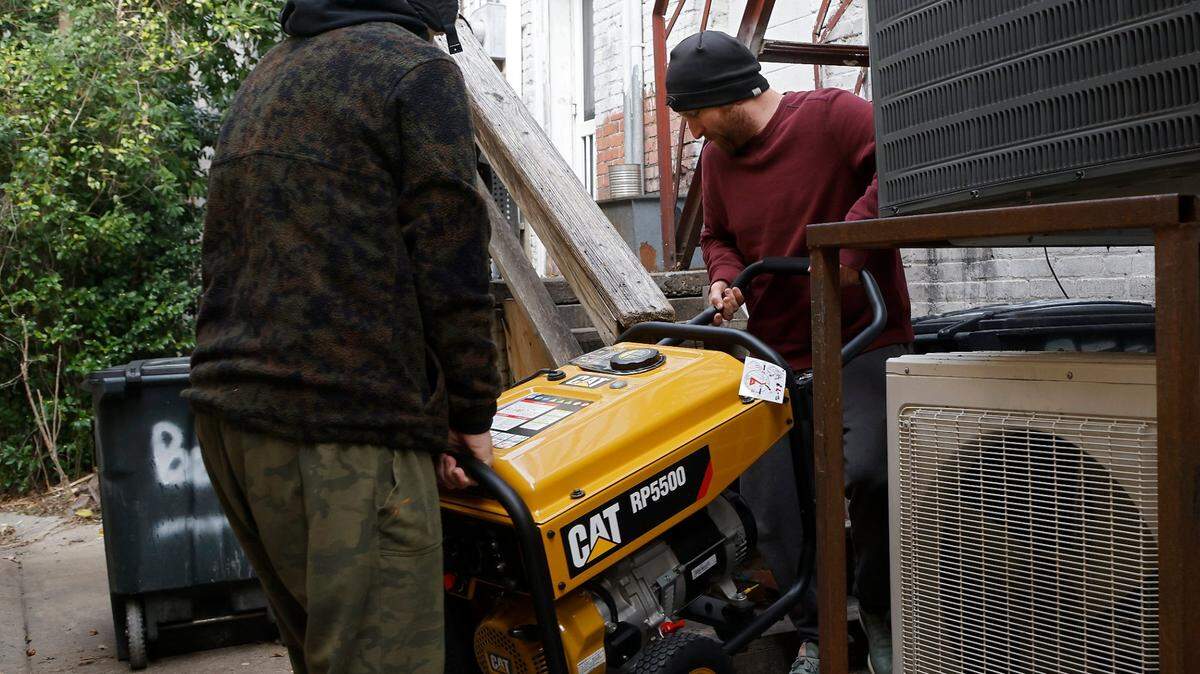 Brothers Tom and Derek Markey carry a portable generator outside of Betsy’s Crepes restaurant on Monday, Dec. 5, 2022, in Southern Pines, N.C. Tom Markey, an employee at the business, said the generator was purchased a few years ago for power outages due to severe weather, but this is its first use.