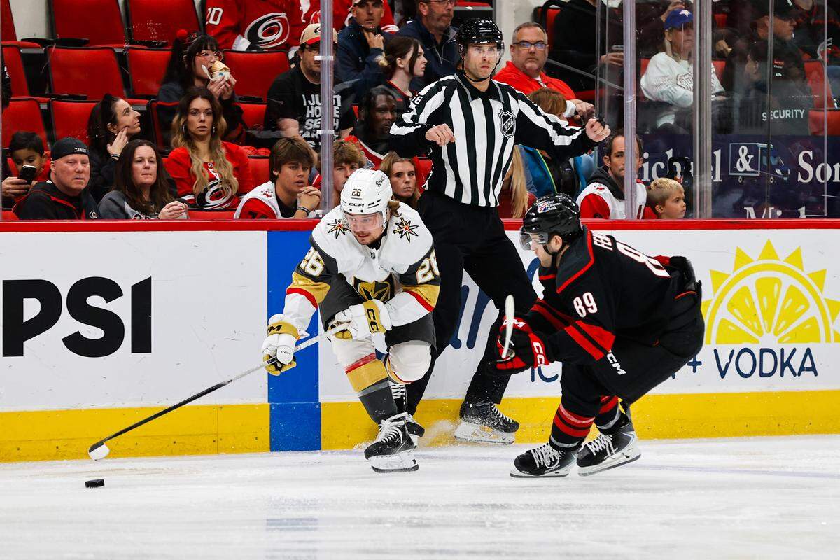 Brett Howden (21) of the Vegas Golden Knights reaches for the puck as Domenick Fensore of the Carolina Hurricanes pursues the play during the first period of the game at the Lenovo Center on October 28, 2025 in Raleigh, North Carolina.