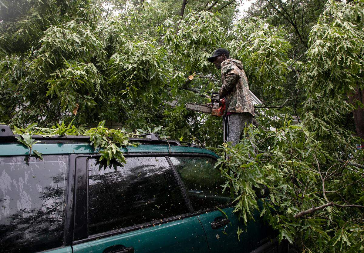 Derrick Parker saws tree limbs from atop a car following strong storms on Monday, May 23, 2022, in Durham, N.C.