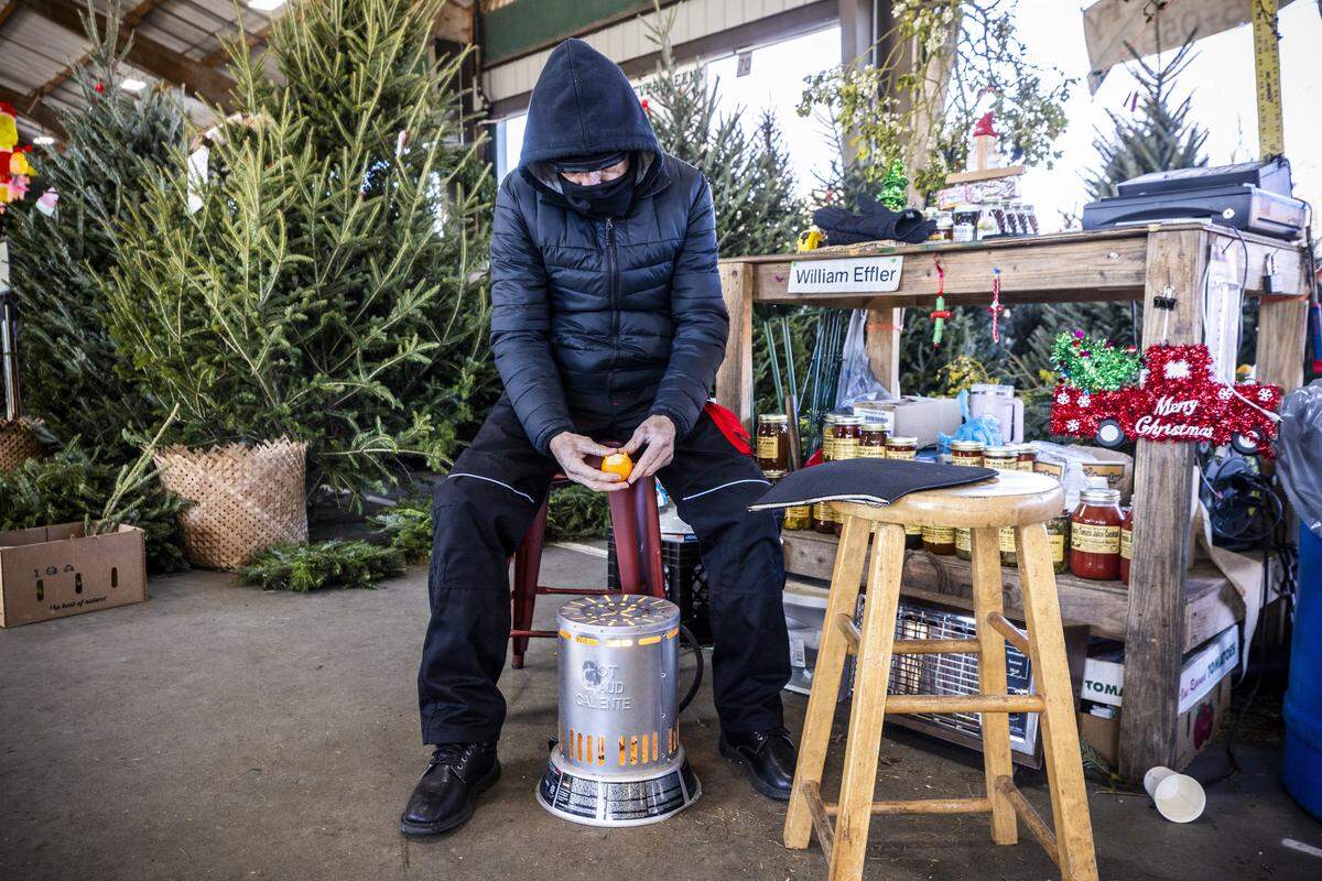 “It gives frozen orange juice a new meaning,” jokes Jimmy Beckwith of Still Fork Nursery and Landscaping in Burnsville as he peels an orange over a propane heater at the company’s Christmas tree vendor stall at the North Carolina State Farmers Market in Raleigh on Monday morning, Dec. 15, 2025. Temperatures in Raleigh dipped into the teens, marking the city’s coldest weather since the winter of 2022.