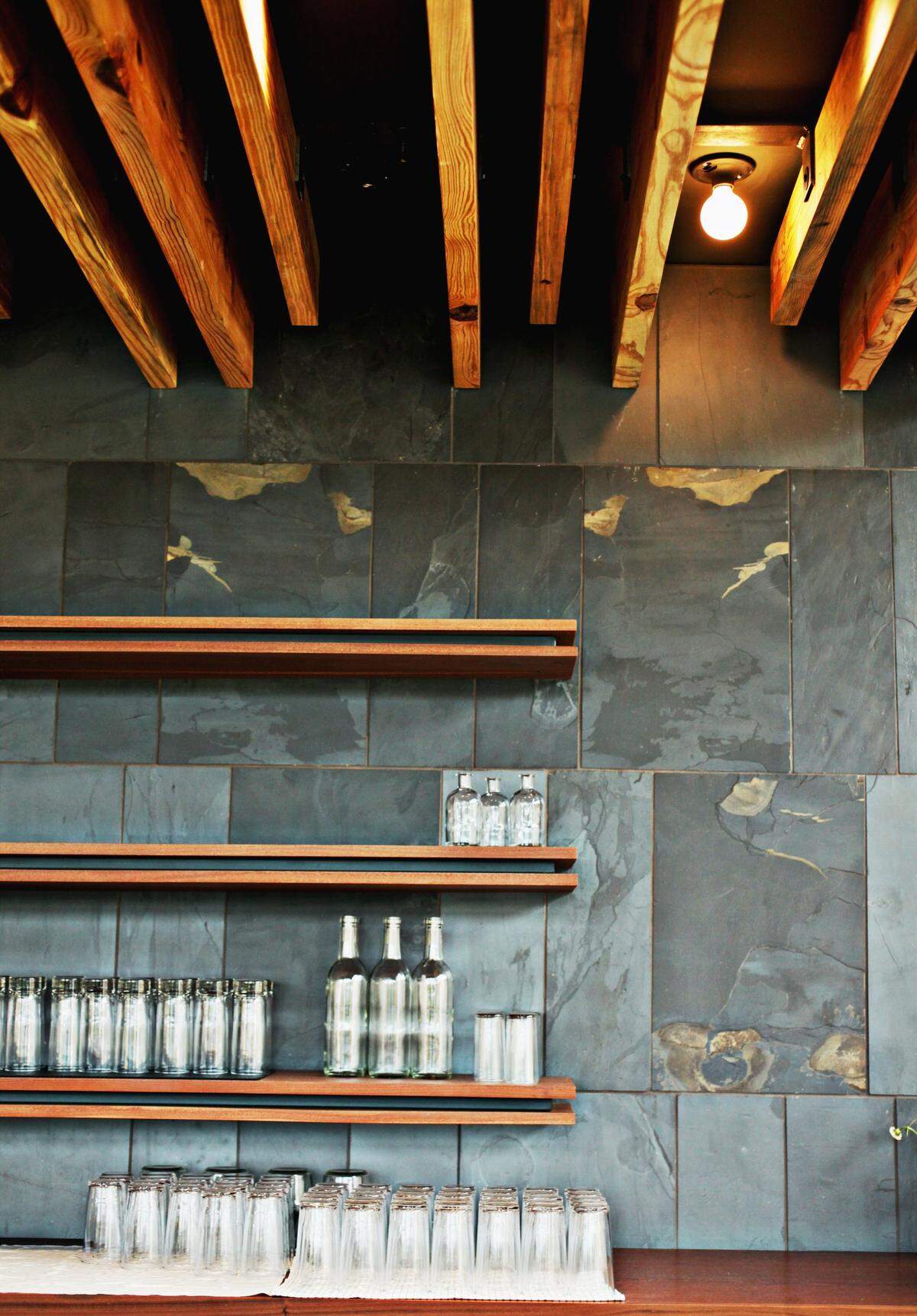 The barcode logo at Standard Beer and Food, photographed in 2015 when it was Standard Foods, is built into the ceiling with wooden beams and appears as a brass inlay on one corner of the marble bar. The Raleigh Architecture Co. designed the shelves and ceiling wood installation and it was built by Arrowhead.
