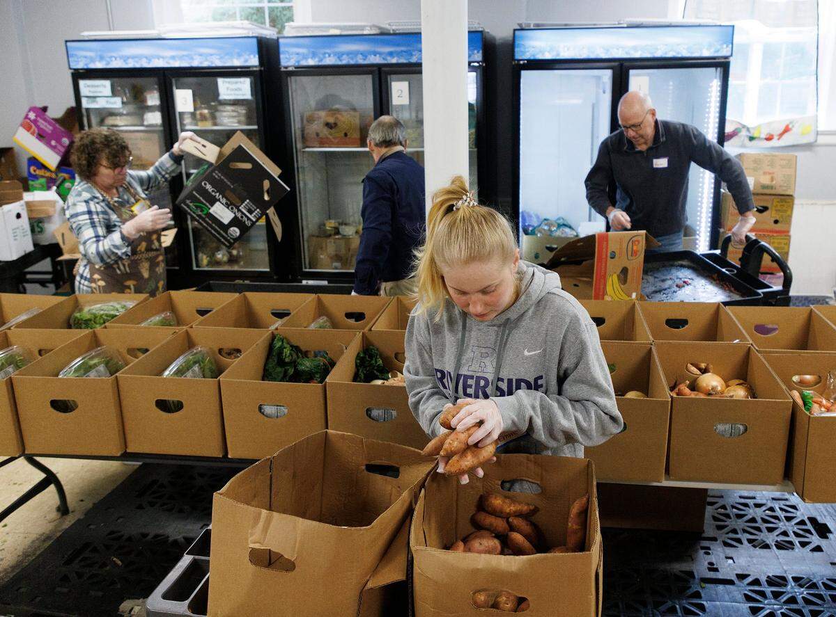 Emma Wilcox, a senior at Riverside High School, adds sweet potatoes to boxes of fresh produce for distribution at a weekly food pantry at Iglesia Presbiteriania Emanuel on Wednesday, Jan. 31, 2024, in Durham, N.C. The food pantry prepared over 50 extra boxes of fresh produce to help accommodate students during the closure of a dozen Durham schools.