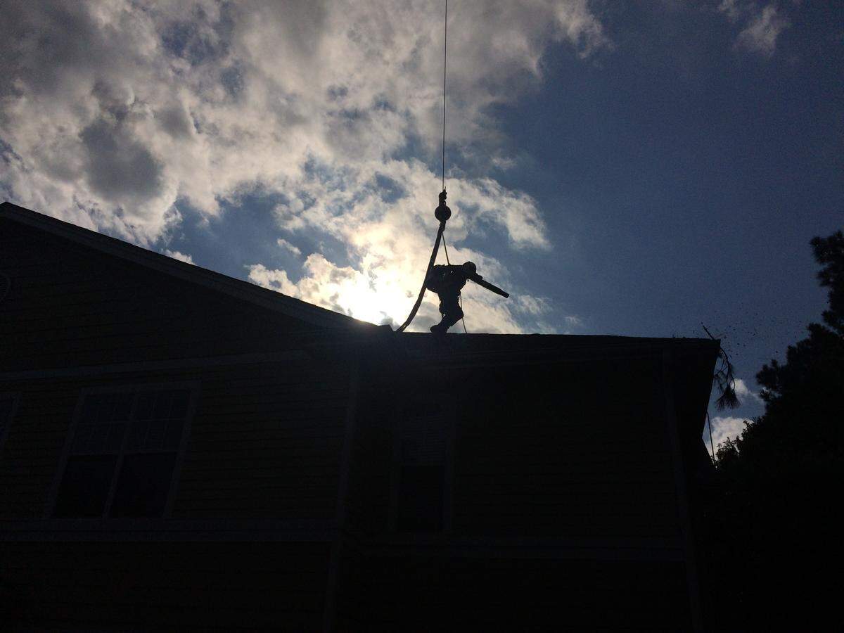 Umberto Castillo dangles from a crane as he blows away the final debris from the roof of a Cary apartment complex after removing a fallen pine tree in the wake of Hurricane Florence on Monday, Sept. 17, 2018.